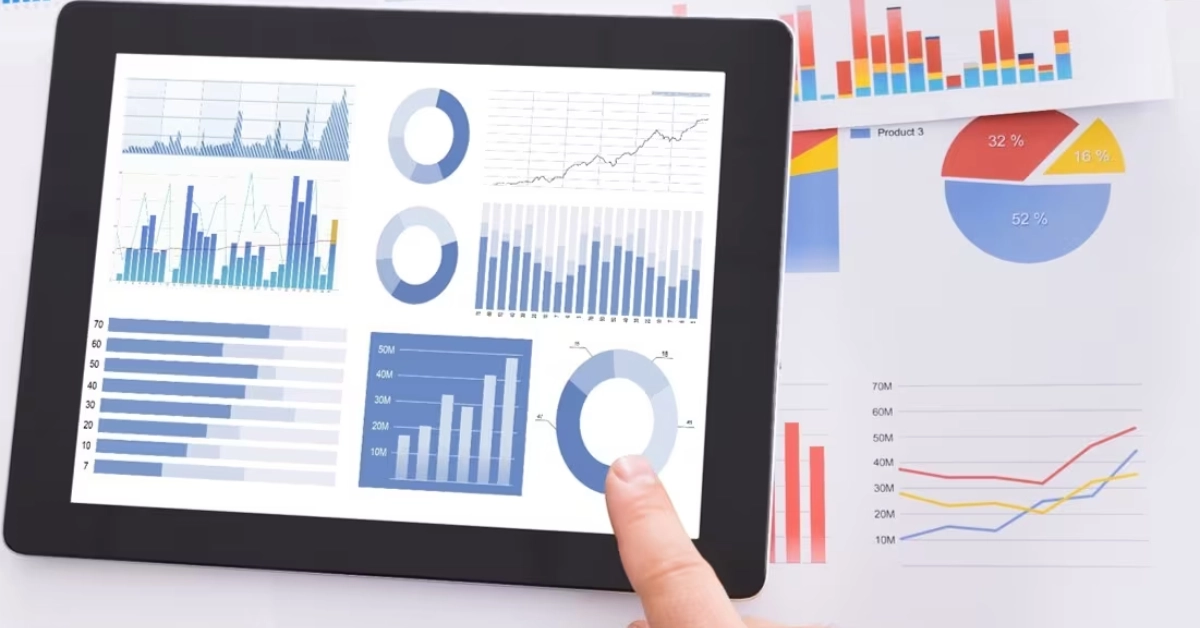 Tablet displaying business analytics charts, graphs, and data reports with printed financial documents in the background for project procurement