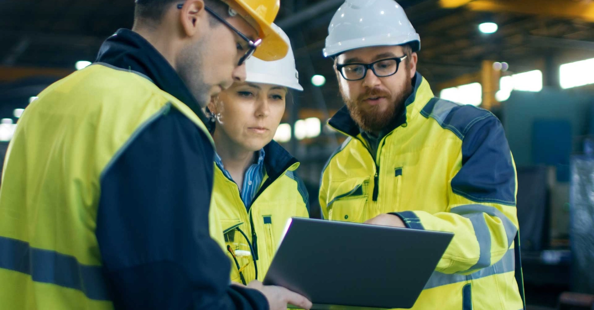 Construction management team reviewing project details on a laptop while wearing hard hats and high visibility workwear