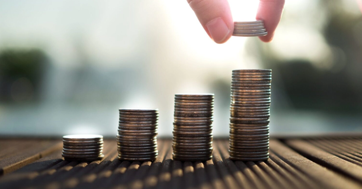 Stacks of coins increasing in height with a hand adding more coins to represent financial growth and investment